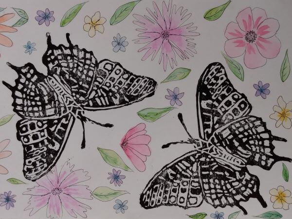 A lino print of butterflies in black ink with painted watercolour flowers in the background