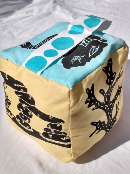 Pale blue and yellow fabric cube doorstop with printed black fish tank ornament shapes on each side